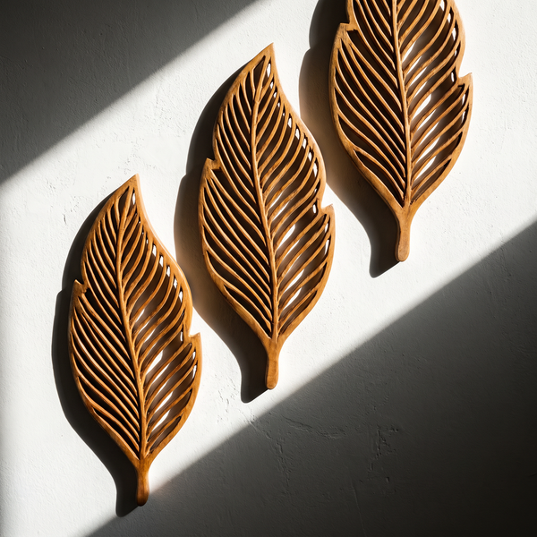 Three carved openwork wooden leaves on a white wall